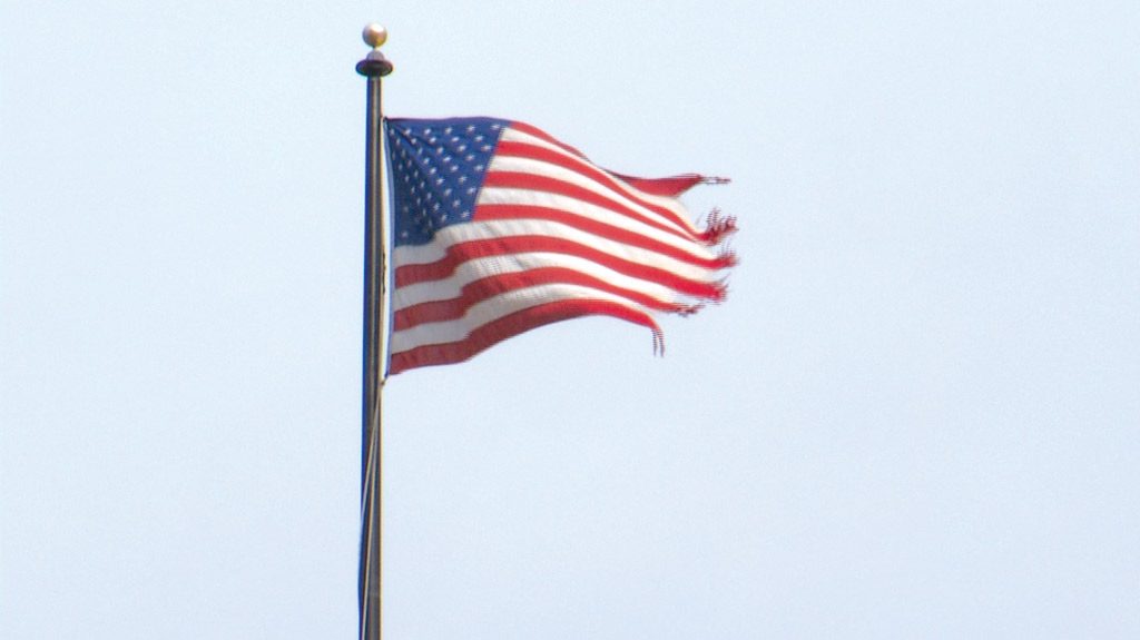 Worn American flag blowing in the wind from a flag pole.