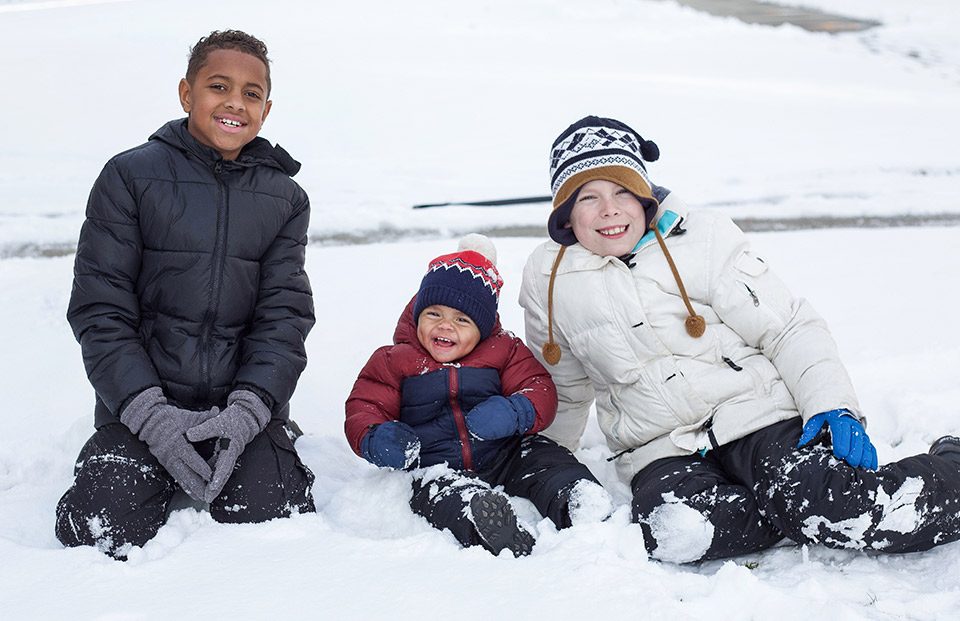 Three kids in winter clothes sitting in the snow.