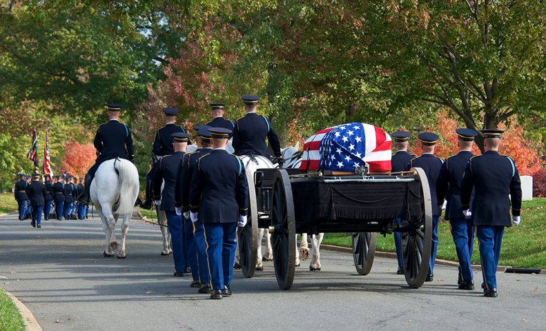 Committal service with horse-drawn wagon carrying casket and uniformed officers walking on both sides.