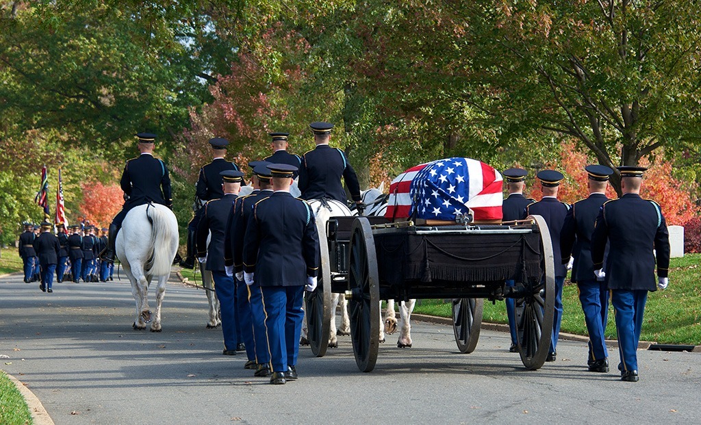 Committal service with horse-drawn wagon carrying casket and uniformed officers walking on both sides.