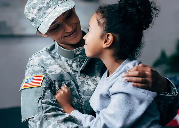 Mom wearing soldier fatigues looking at young daughter in her arms.