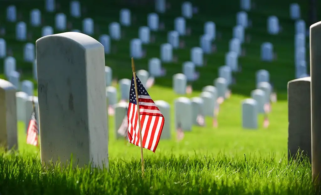 Cemetery headstone with American flag next to it.
